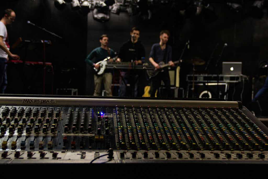 Travail en studio, table de mixage et 3 musiciens en arrière plan